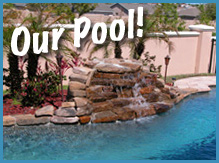 A swimming pool with a rock waterfall feature and surrounding plants. The words "Our Pool!" are written in white text at the top. A wall and houses are visible in the background.