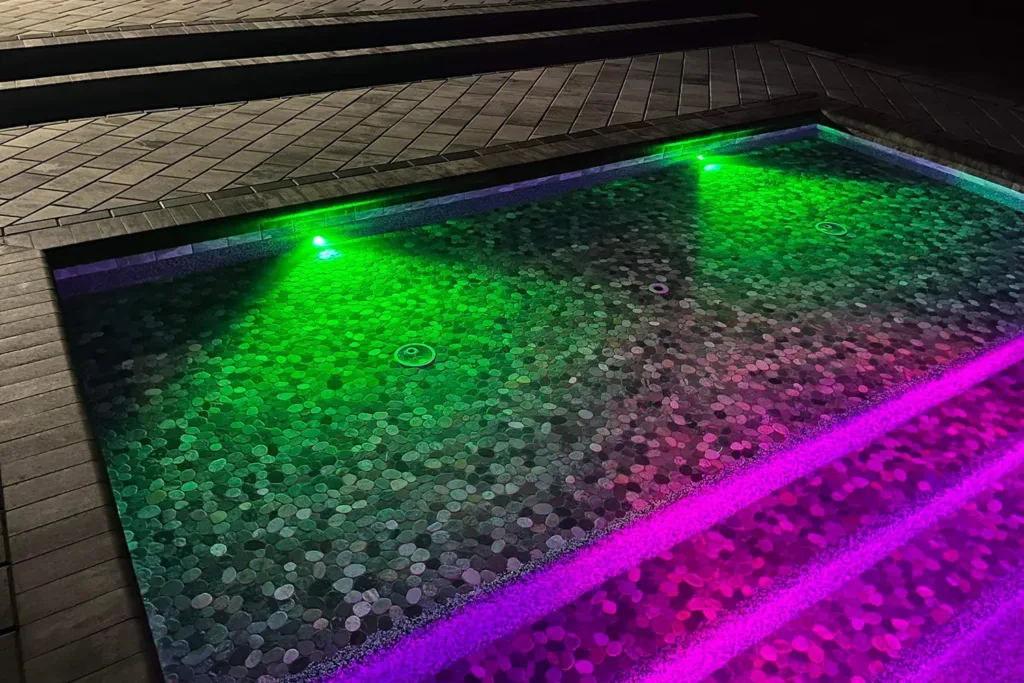 Custom pool lit with green and purple LED lighting at night