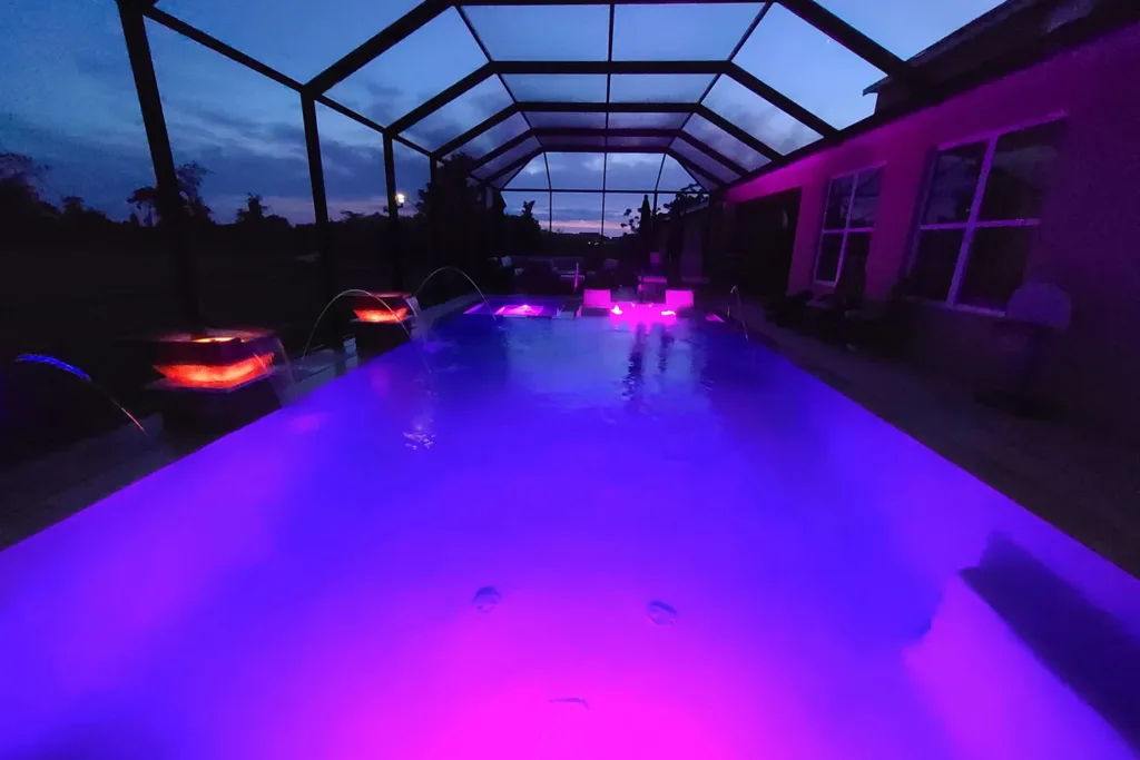 Screened pool glowing with purple LED lighting and fire bowls at night