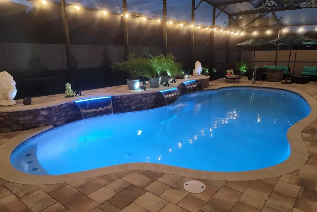Free-form pool with LED lighting and string lights inside a screened lanai at dusk