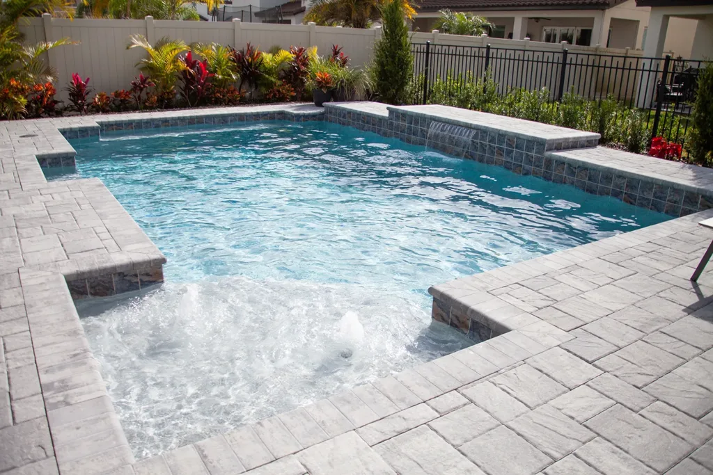 Custom pool with a sun shelf, raised spa and paver deck surrounded by tropical landscaping