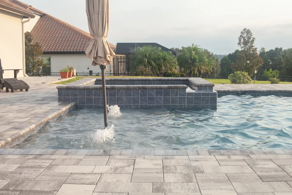 Custom pool with a raised spa spillover and a paver deck in the afternoon sun
